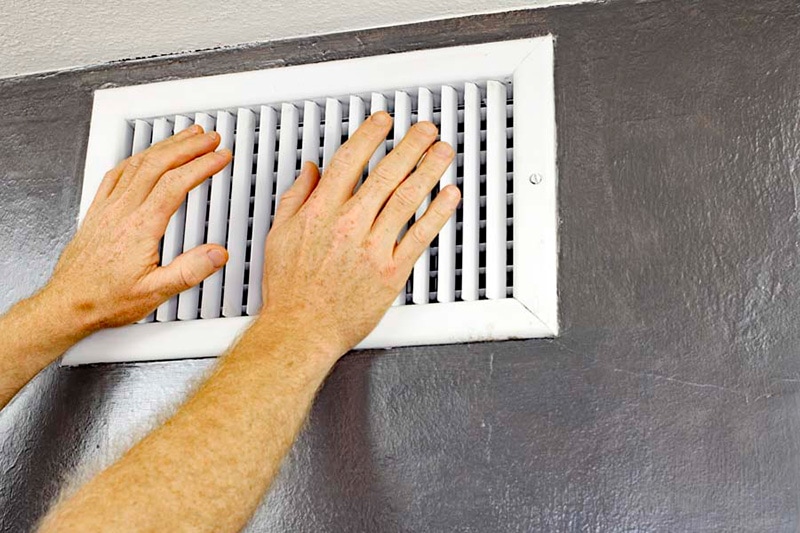 Hands against an air vent blowing warm air, Why is My Air Conditioner Blowing Hot Air? | Comfortable Design