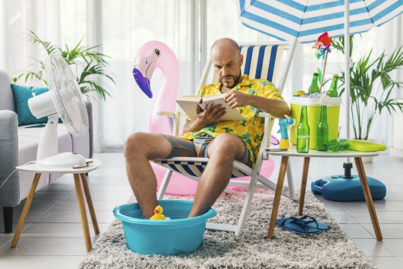 3 Signs It’s Time for a New AC. Man in his living room sitting on a deckchair with his feet in a mini pool reading a book.