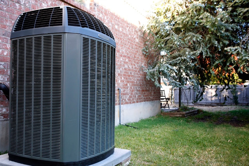 Close up of outdoor AC unit against a brick wall, Four Things to Know About Your Air Conditioner | Comfortable Design Inc.